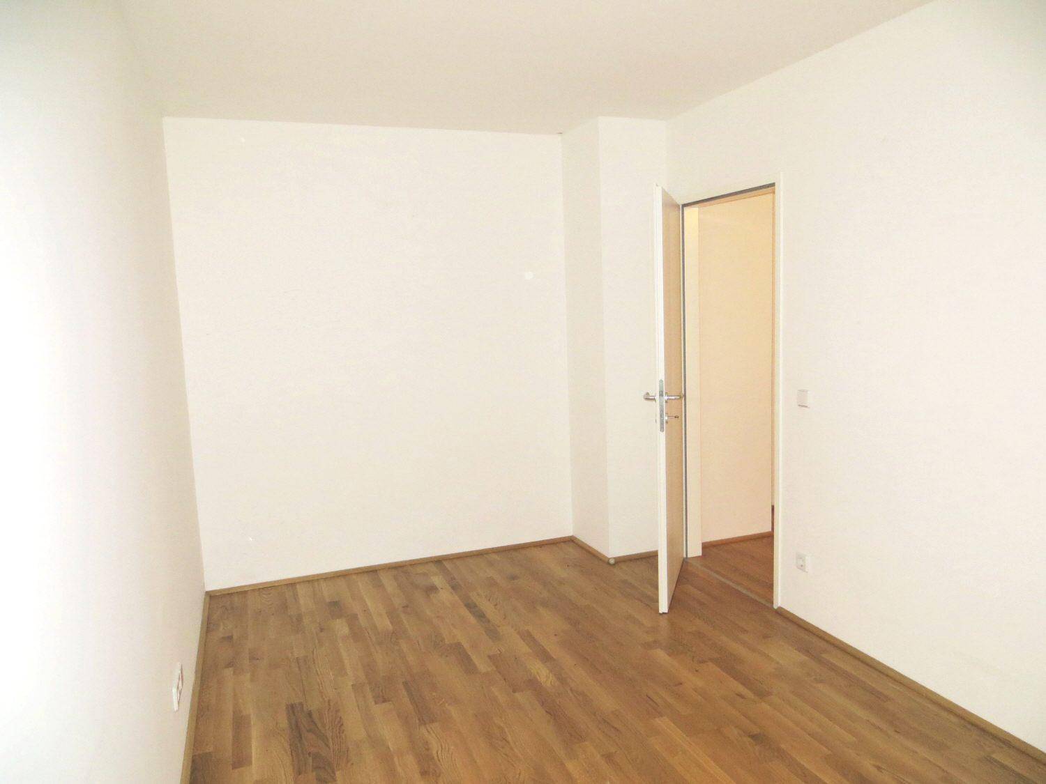 Leeres Zimmer mit hellem Parkettboden und weiß gestrichenen Wänden.