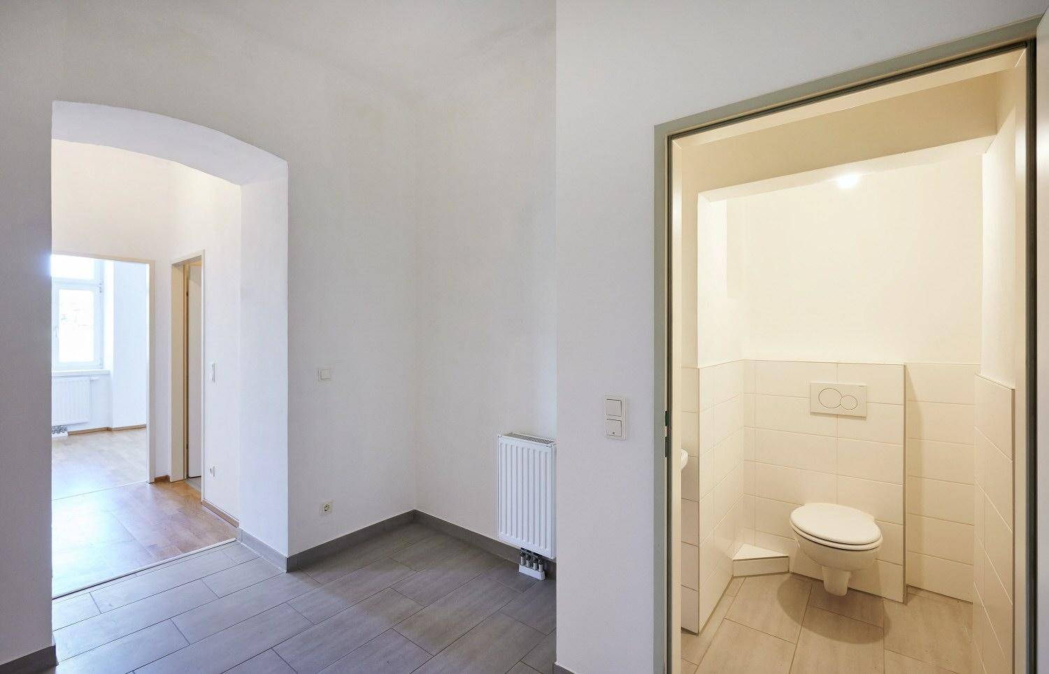 Flur mit Fliesenboden und Zugang zu einer separaten Gästetoilette mit Wand-WC.