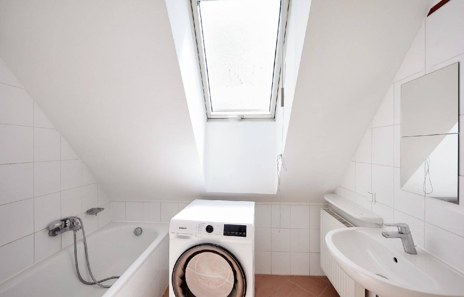 Dachgeschoss-Badezimmer mit Badewanne, Waschmaschine und Dachfenster für natürliches Licht.