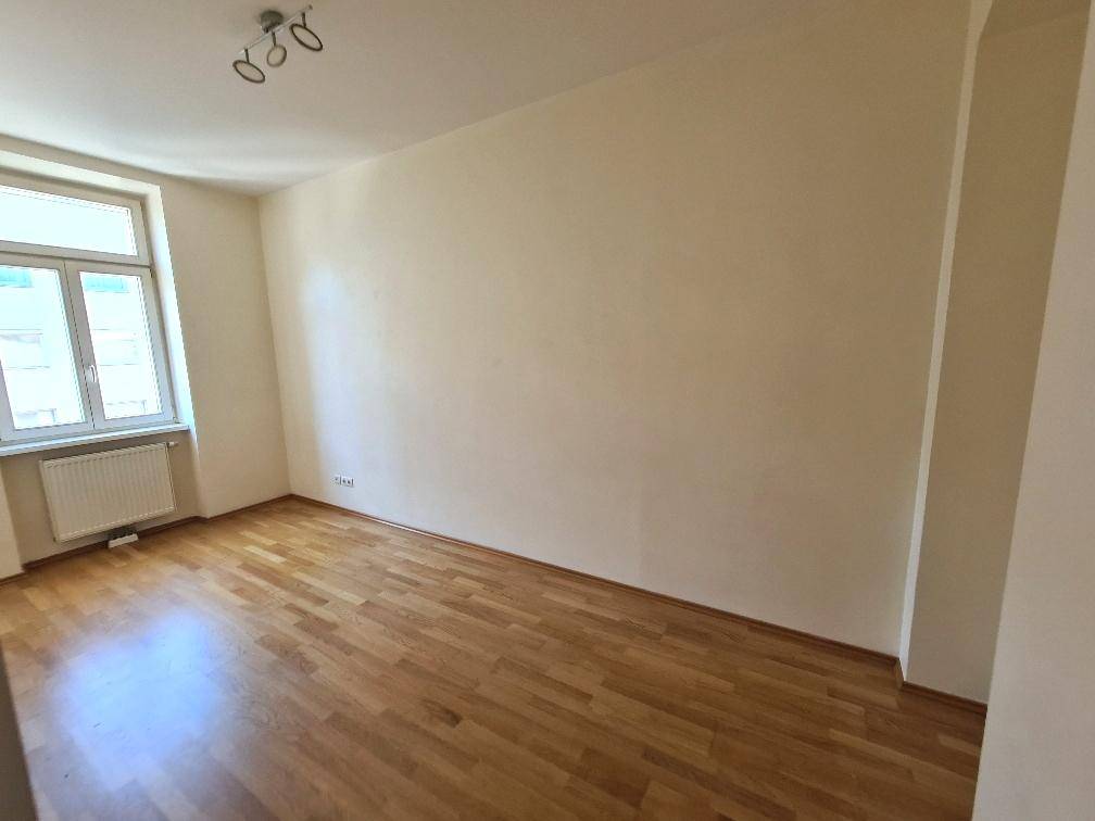 Helles Zimmer mit Parkettboden und einem Fenster, ideal als Schlaf- oder Arbeitszimmer.