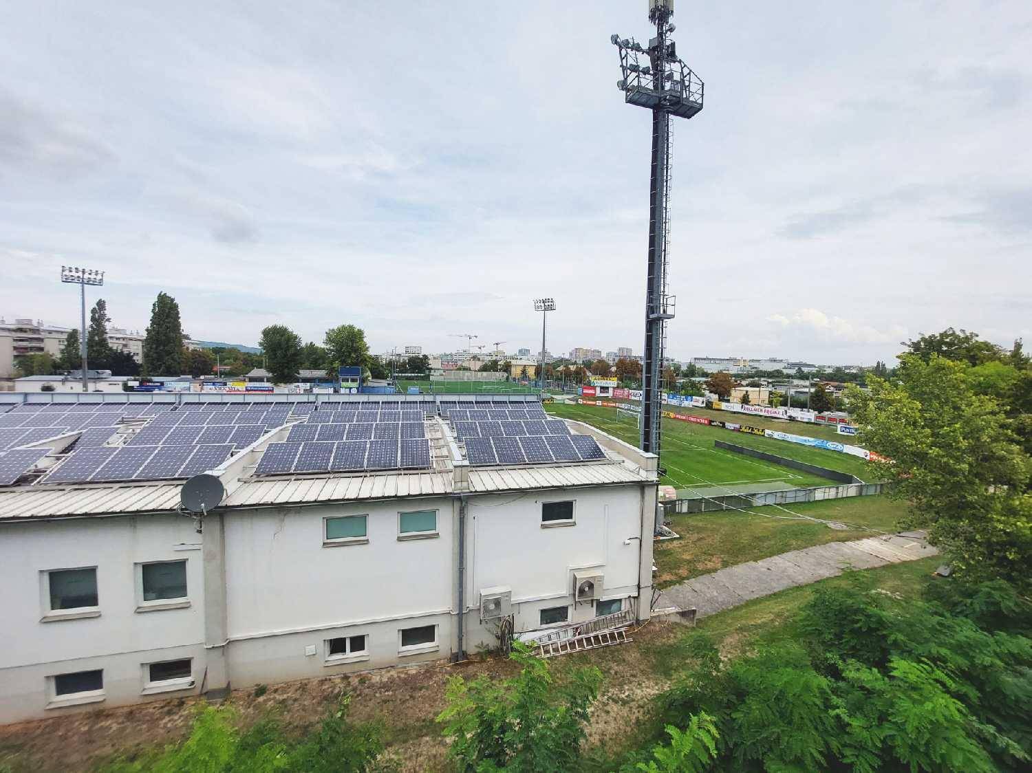 Blick auf ein Stadion mit Solaranlagen auf dem Dach und die städtische Umgebung.