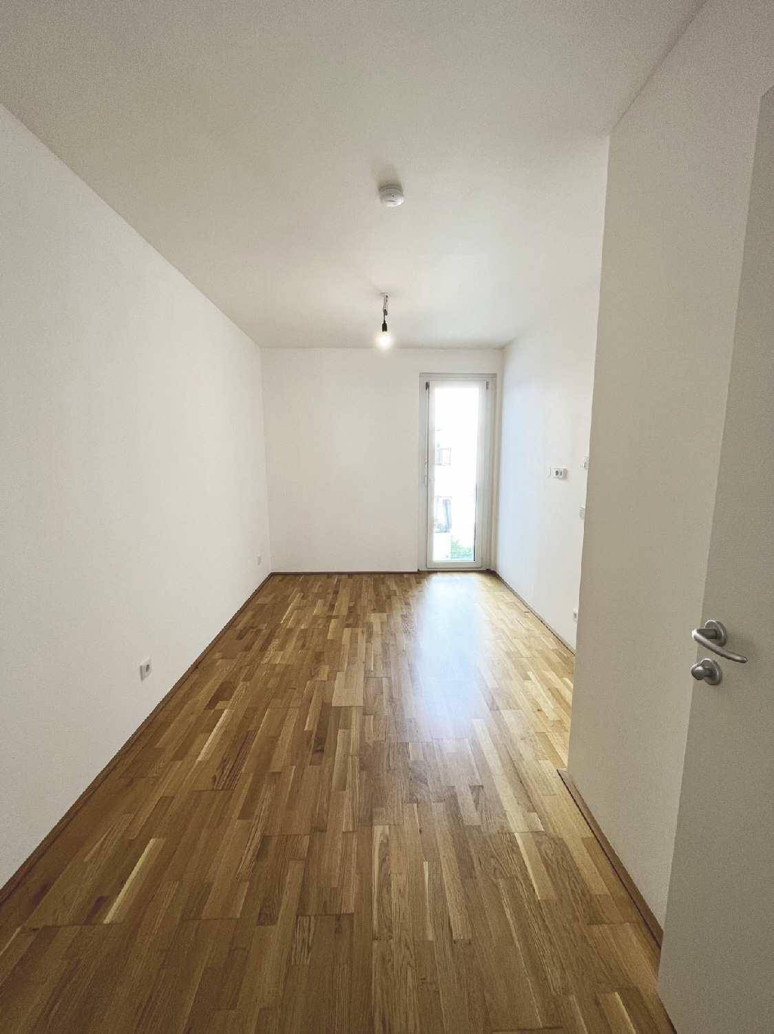 Helles Zimmer mit Parkettboden und einer Tür, die zu einem weiteren Bereich führt.