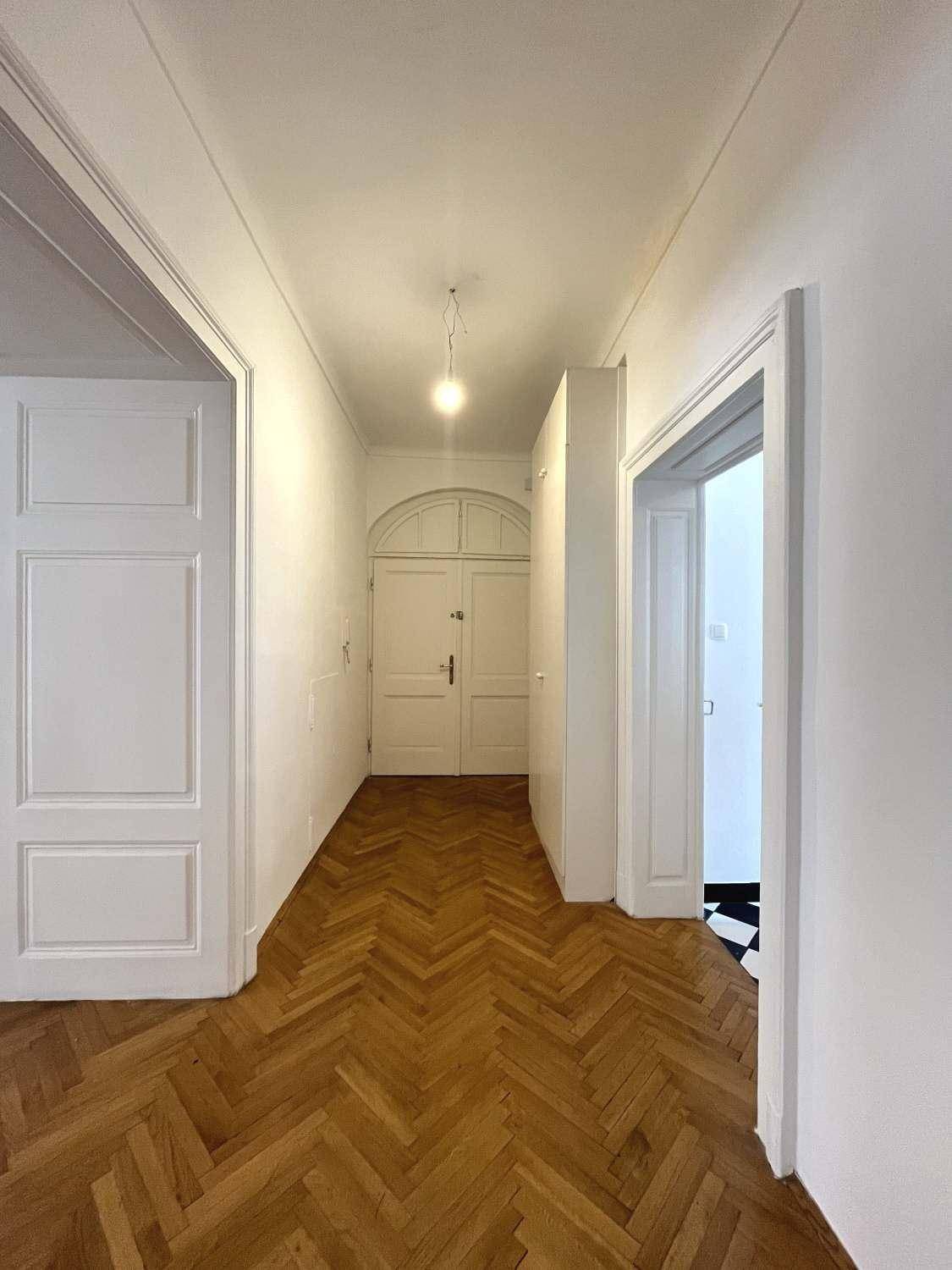 Langer Flur mit Fischgrätparkett und hohen Decken, der zu verschiedenen Räumen führt.