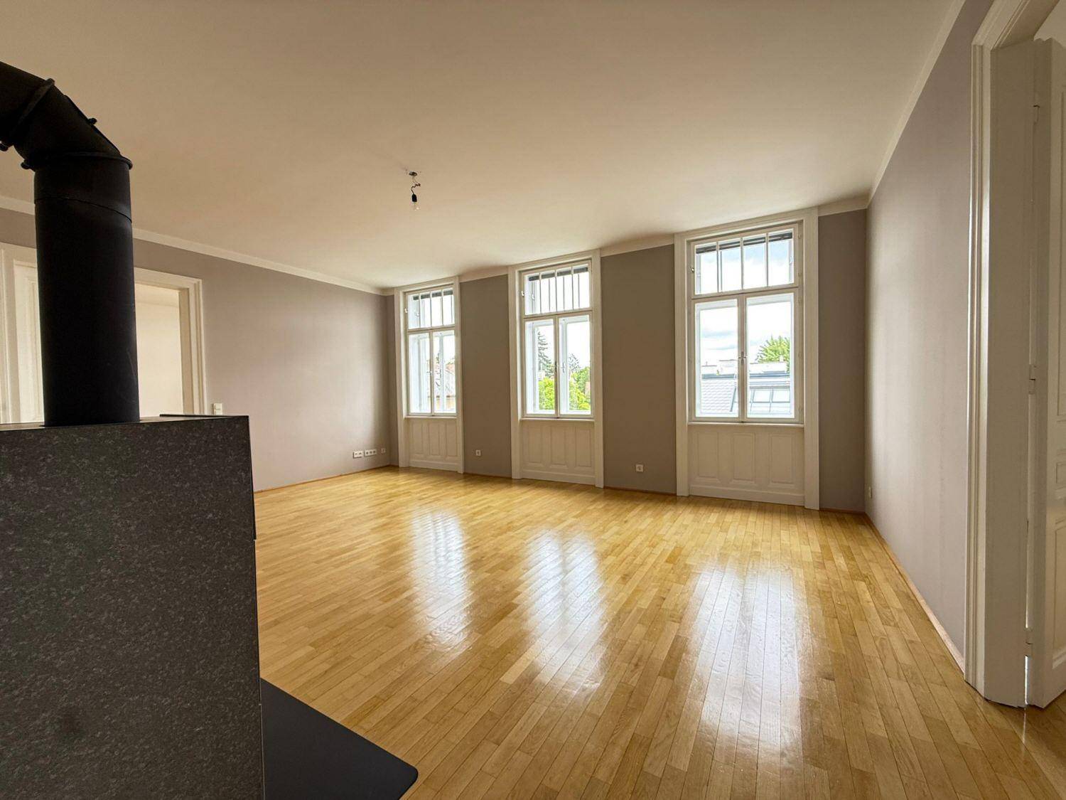 Großzügiges Wohnzimmer mit Parkettboden, Kaminofen und hohen Fenstern für viel Licht.