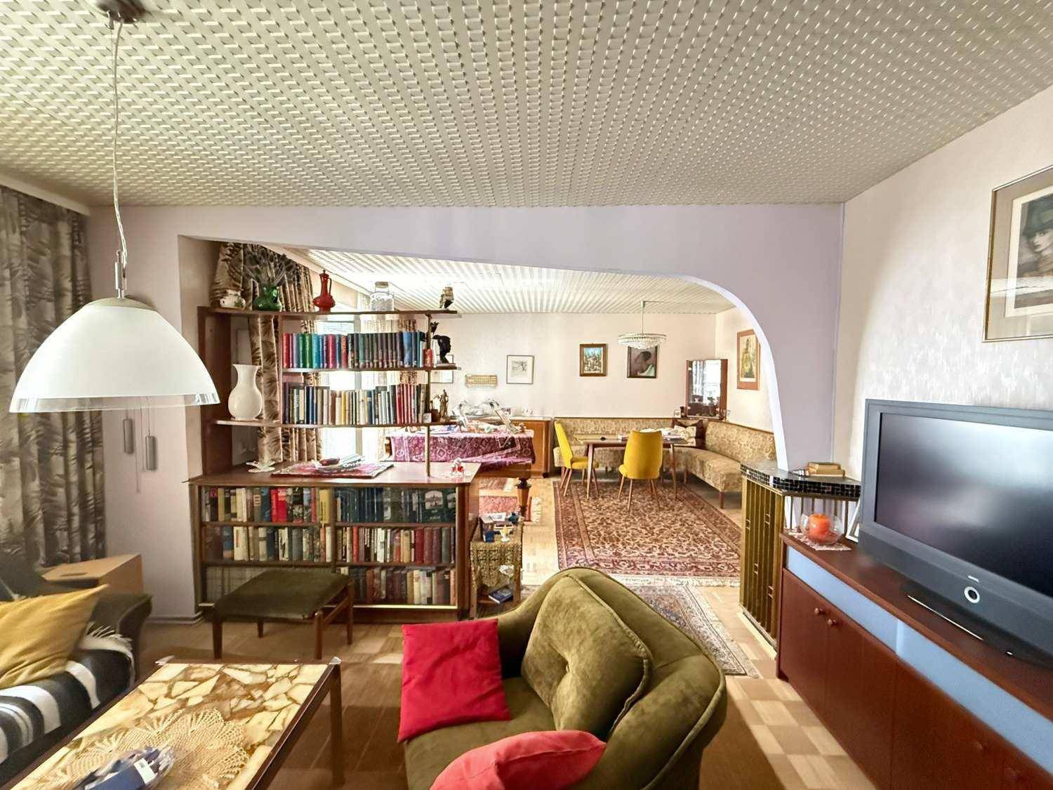 Geräumiger Wohn- und Essbereich mit bequemen Sofas, Bücherregalen und einem Essbereich im Hintergrund.