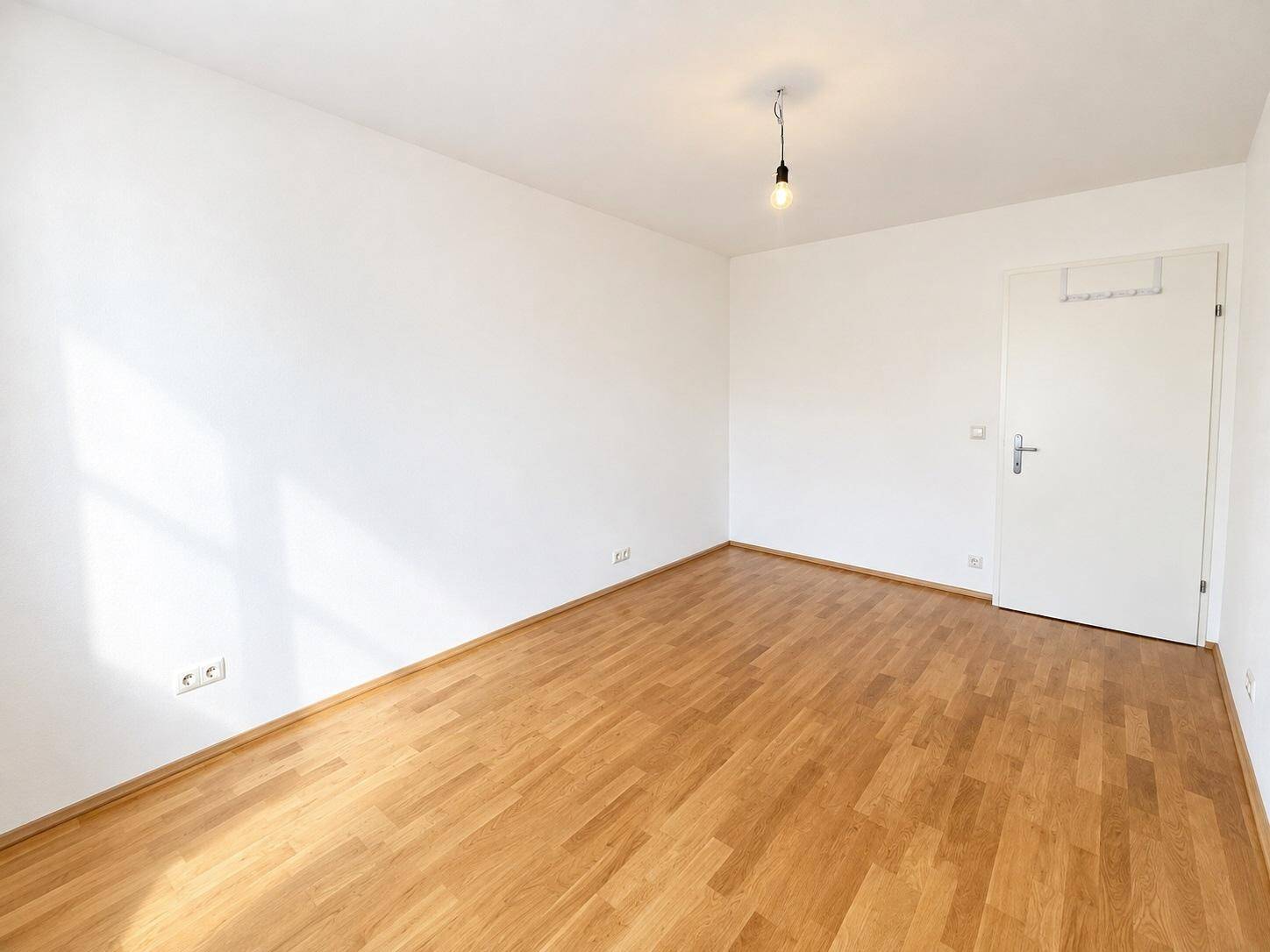 Helles Zimmer mit Parkettboden und weißen Wänden, bereit zur individuellen Gestaltung.