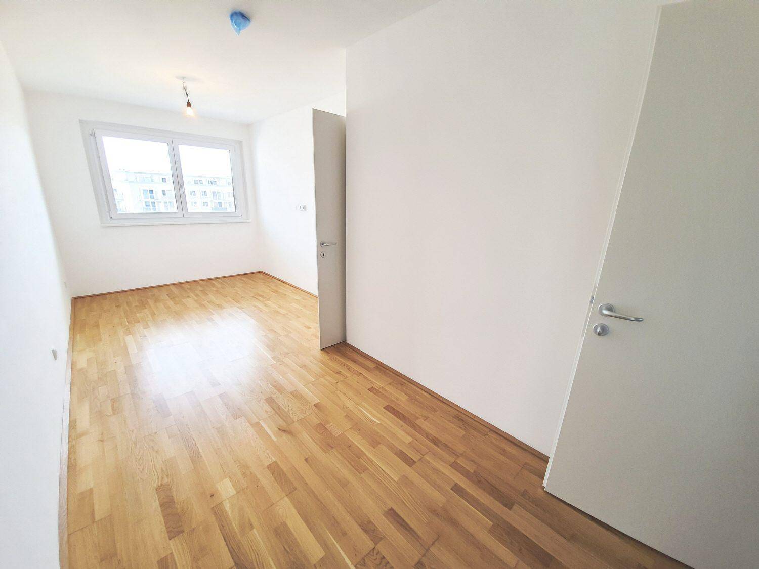 Helles Schlafzimmer mit Parkettboden, weißen Wänden und einem großen Fenster für viel Tageslicht.