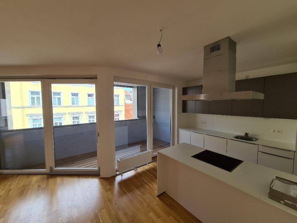 Offener Wohn- und Küchenbereich mit Kochinsel, Parkettboden und Zugang zum Balkon.