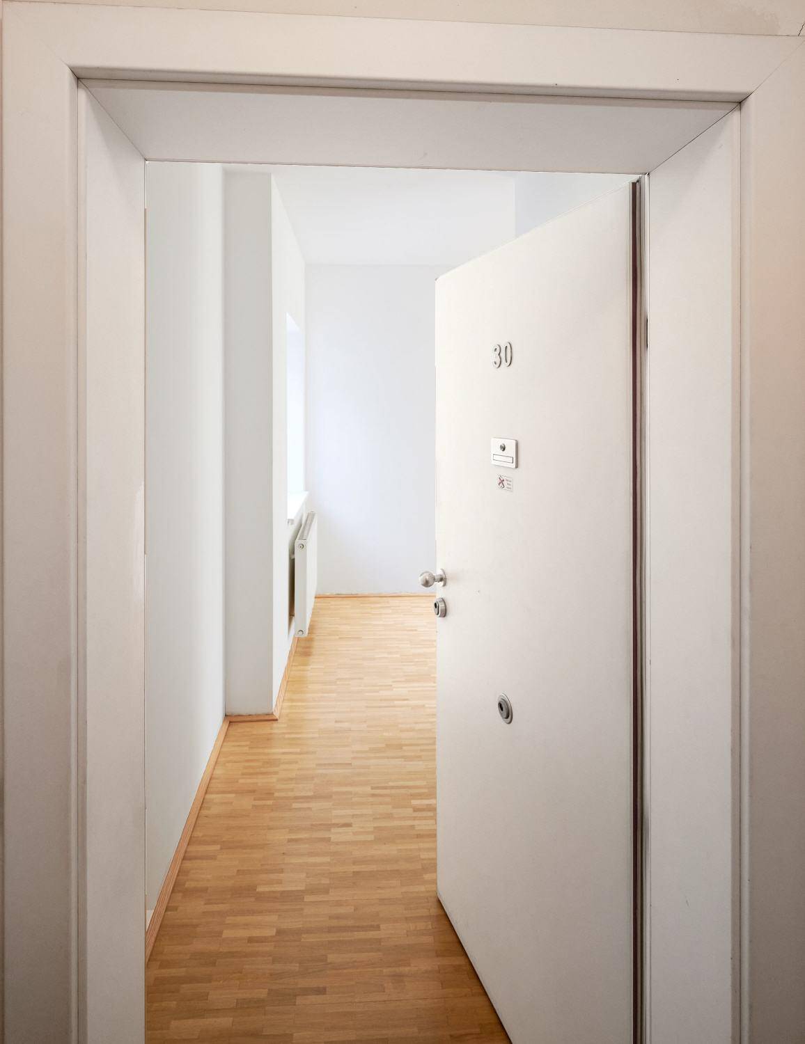 Eingangsbereich mit offener Tür zu einem hellen Flur mit Holzboden.