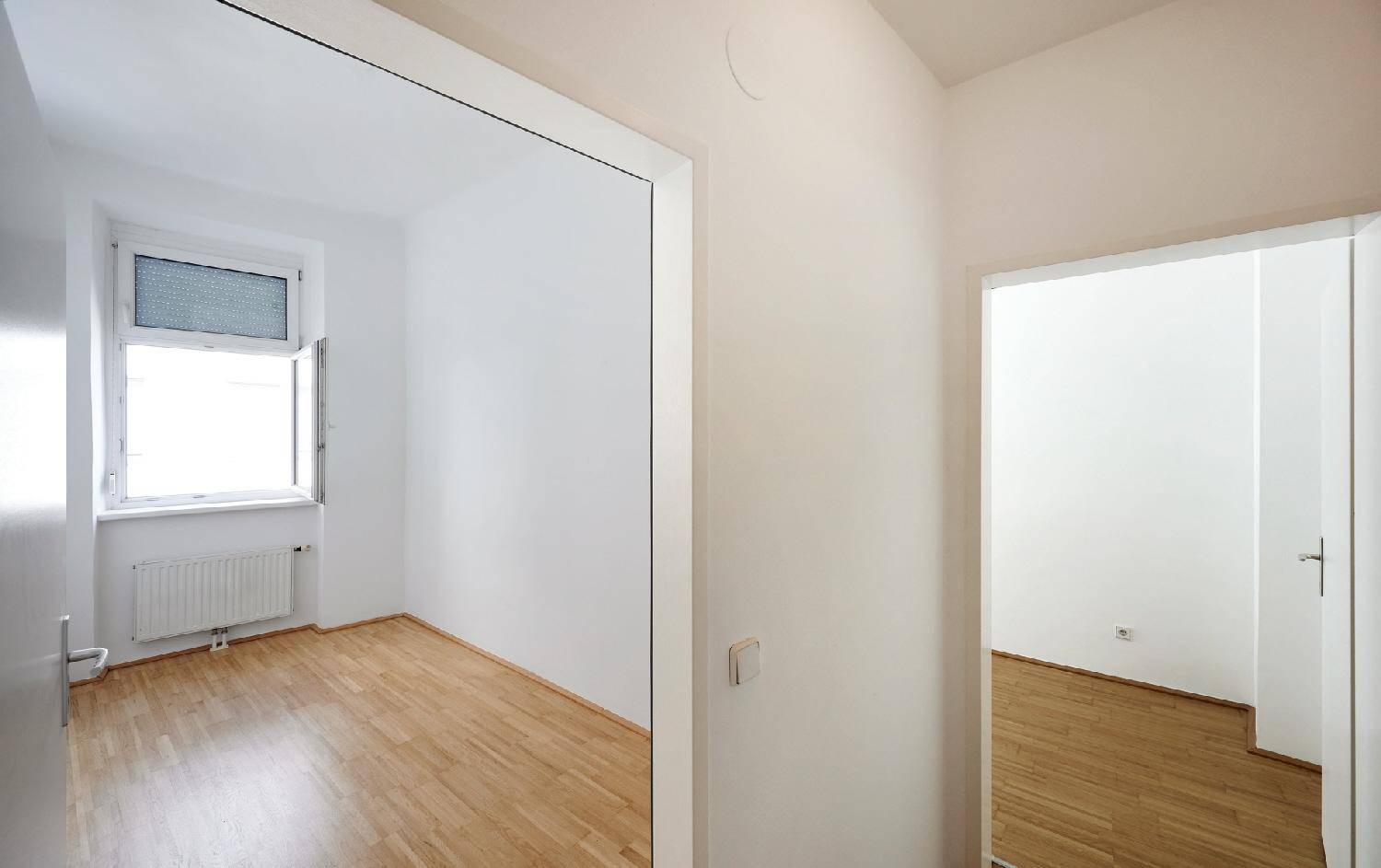 Flur mit Parkettboden und Zugang zu einem hellen Zimmer mit Fenster.