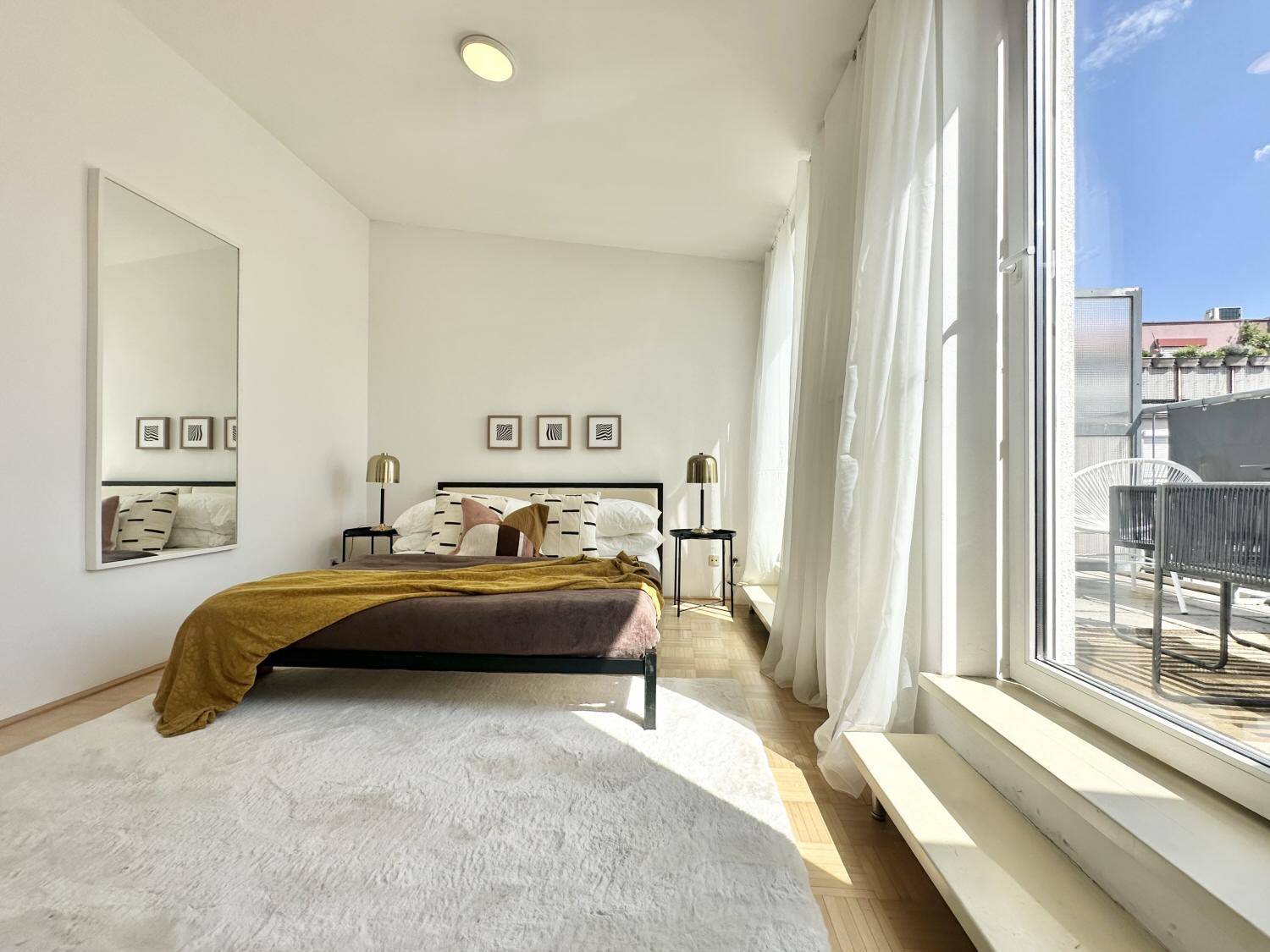 Helles Schlafzimmer mit großem Bett, Spiegel und Zugang zum sonnigen Balkon.