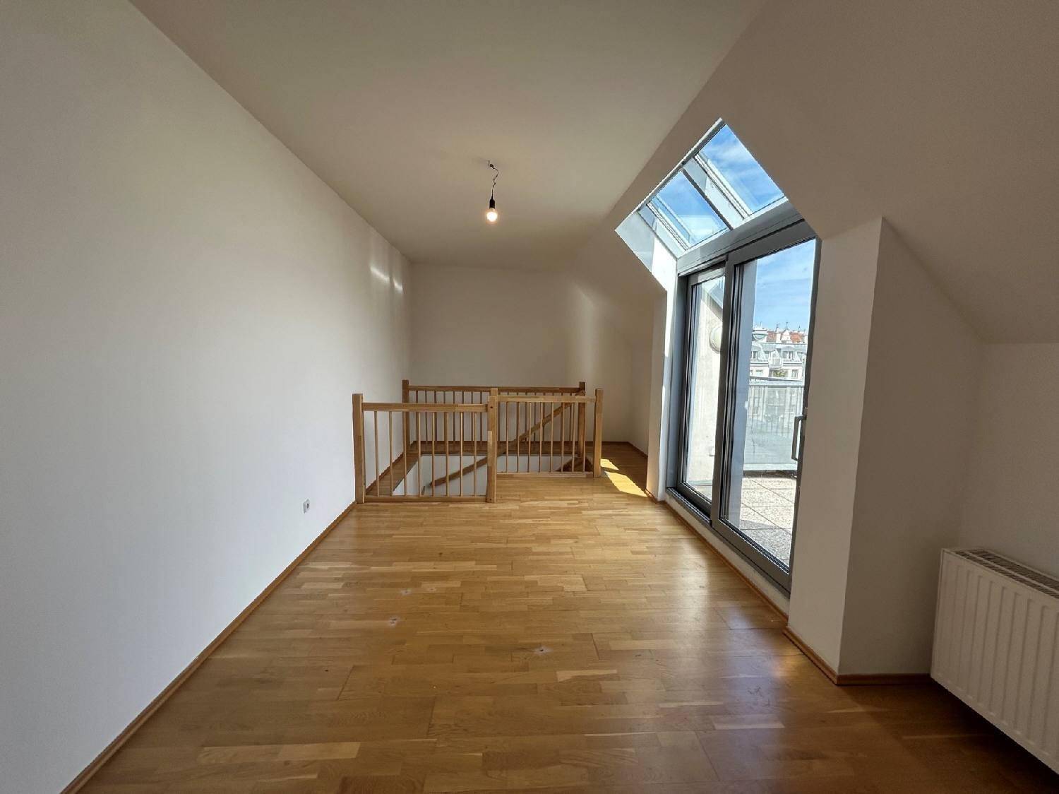 Lichtdurchfluteter Dachgeschossraum mit Holzboden und Zugang zu einer Terrasse durch große Fenster.