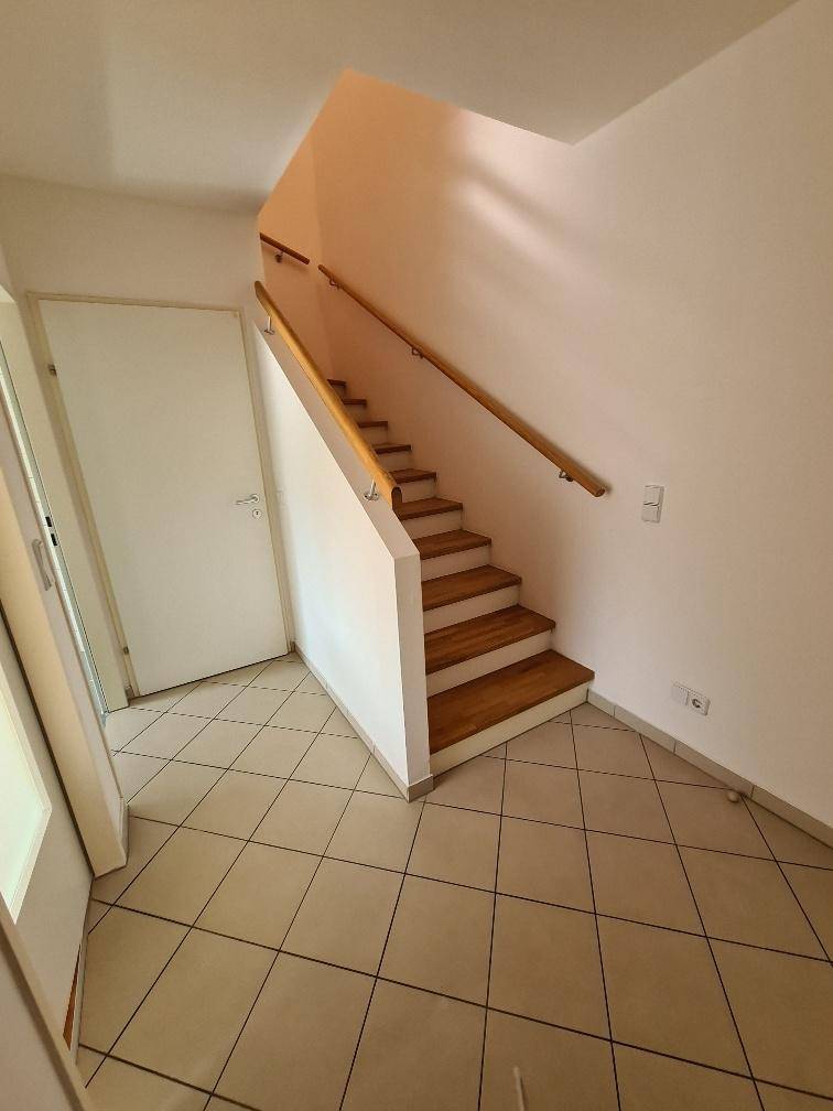 Heller Flur mit Fliesenboden und einer Holztreppe, die in die obere Etage führt.