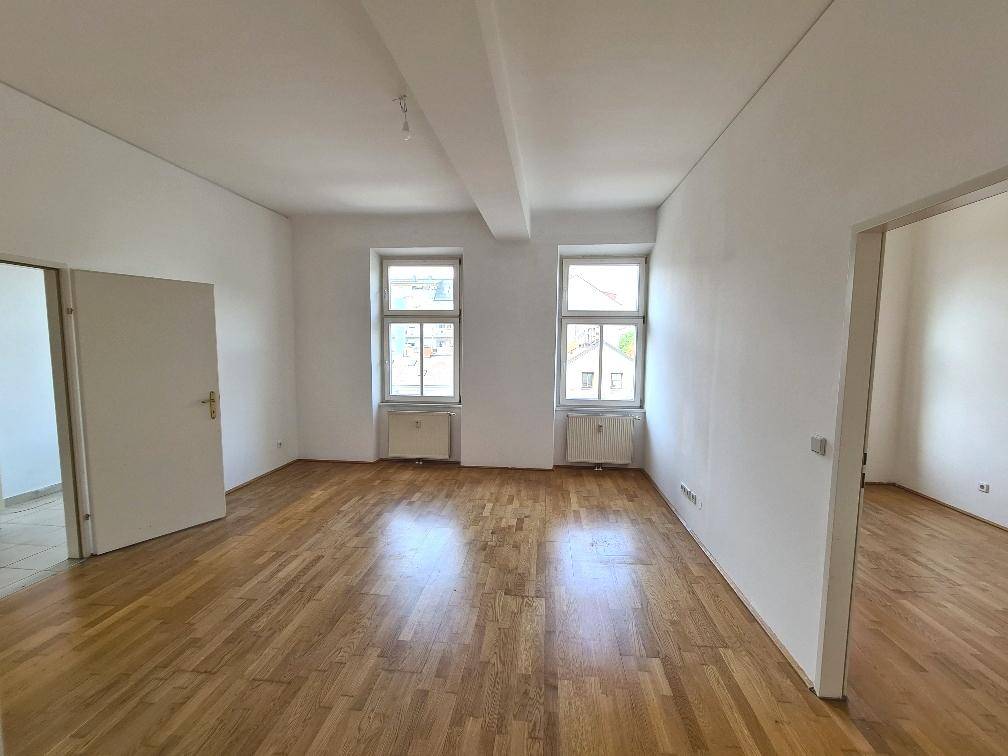 Heller, leerer Raum mit Parkettboden und zwei Fenstern, bereit zur individuellen Gestaltung.
