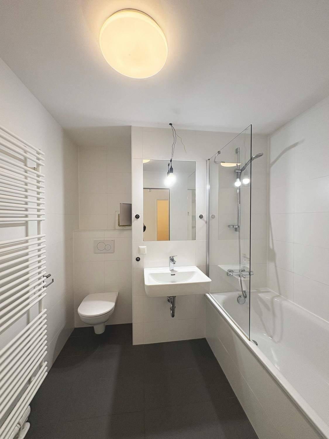 Modernes Badezimmer mit Badewanne, Duschwand, wandhängendem WC und beheiztem Handtuchhalter für Komfort.