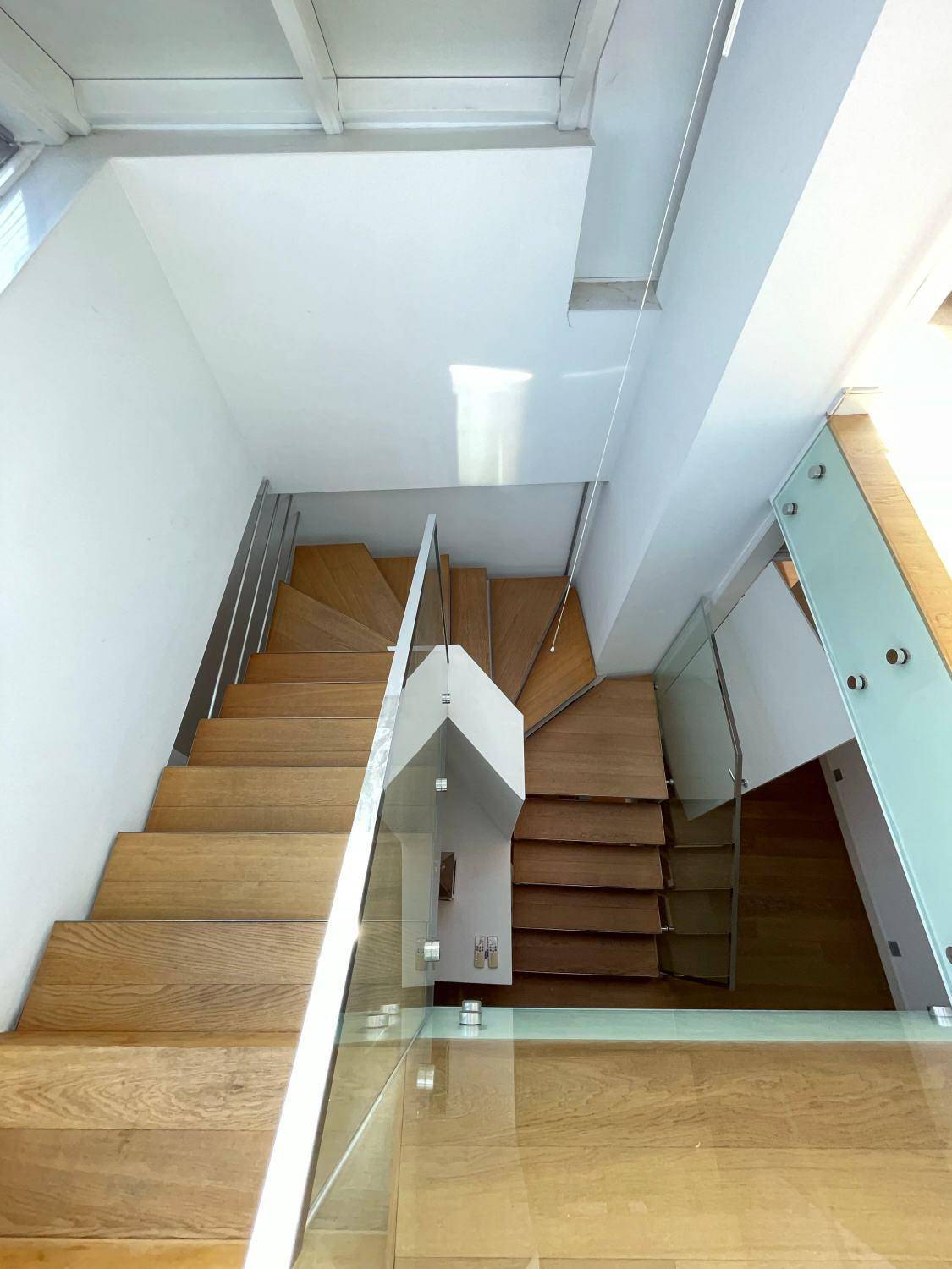 Moderne Holztreppe mit Glasgeländer, die verschiedene Ebenen des Hauses stilvoll verbindet.