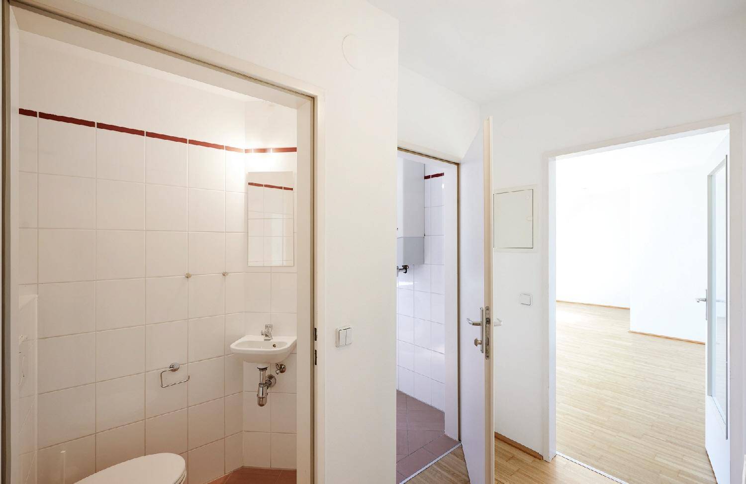 Flur mit Zugang zu einem Gäste-WC und einem Badezimmer, beide mit Fliesenboden.