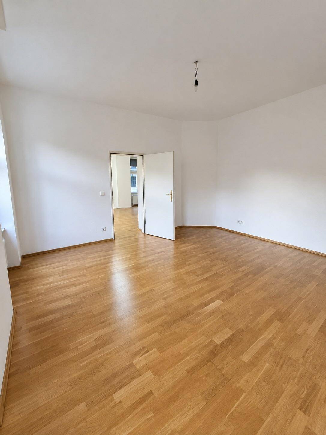 Heller Wohnraum mit Parkettboden und einer offenen Tür, die zu einem weiteren Zimmer führt.