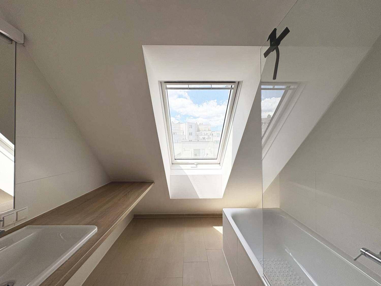Modernes Badezimmer mit Badewanne, Waschtisch und Dachfenster unter einer Dachschräge.