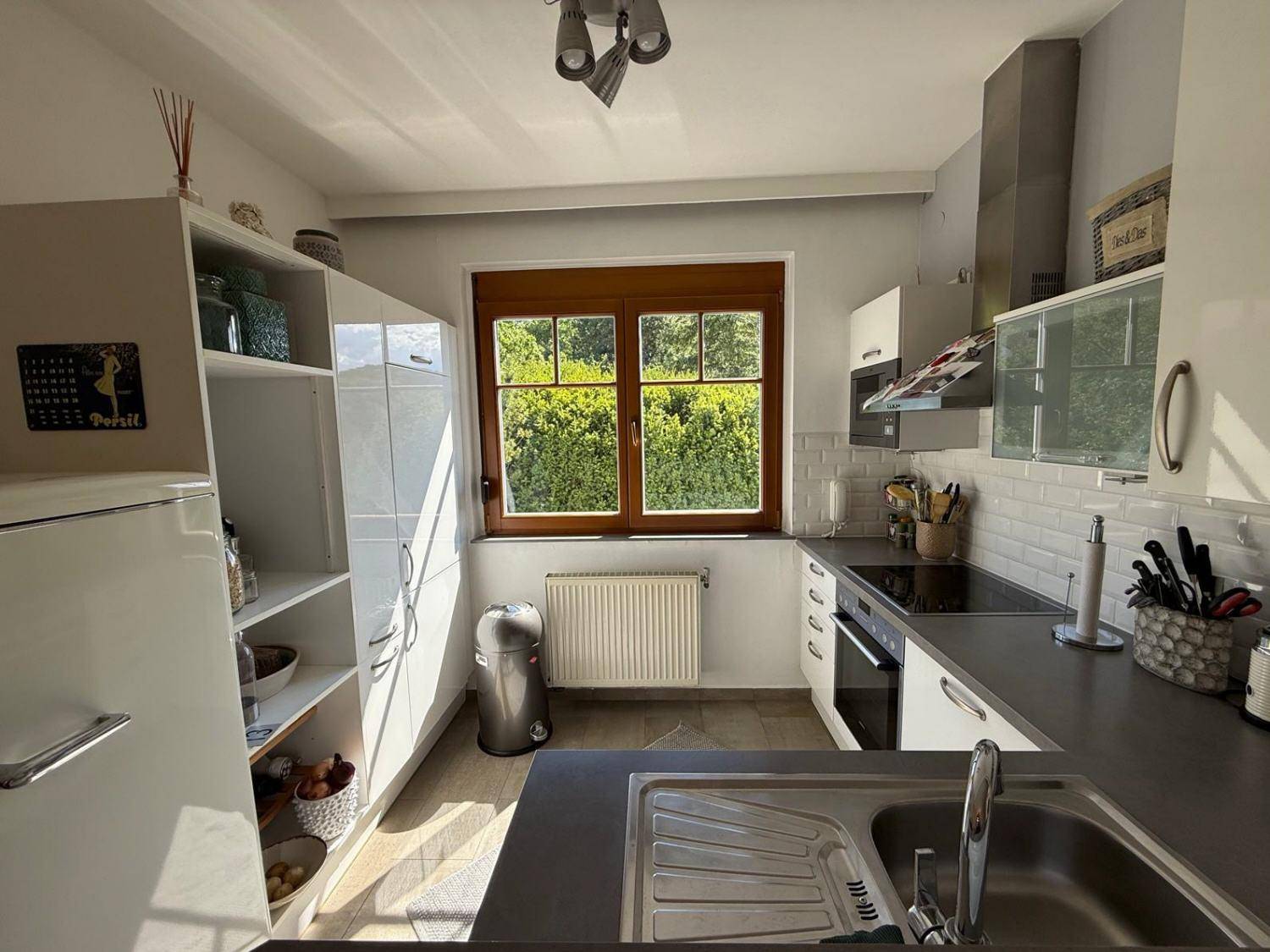 Helle Küche mit weißen Schränken, dunkler Arbeitsplatte und Fenster zum Garten.