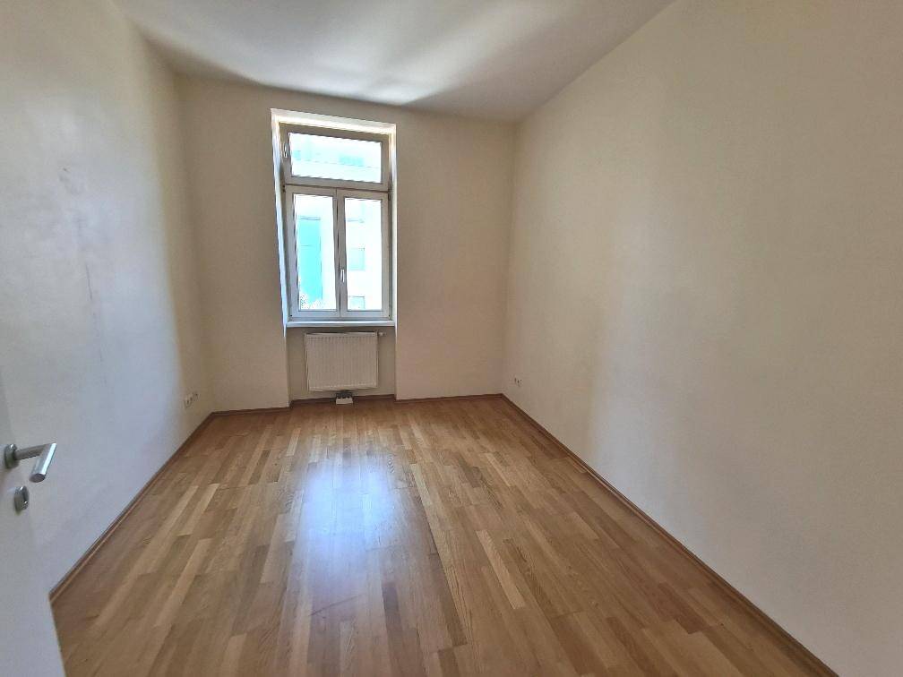 Ruhiges Zimmer mit Parkettboden und Fenster, geeignet als Schlaf- oder Kinderzimmer.