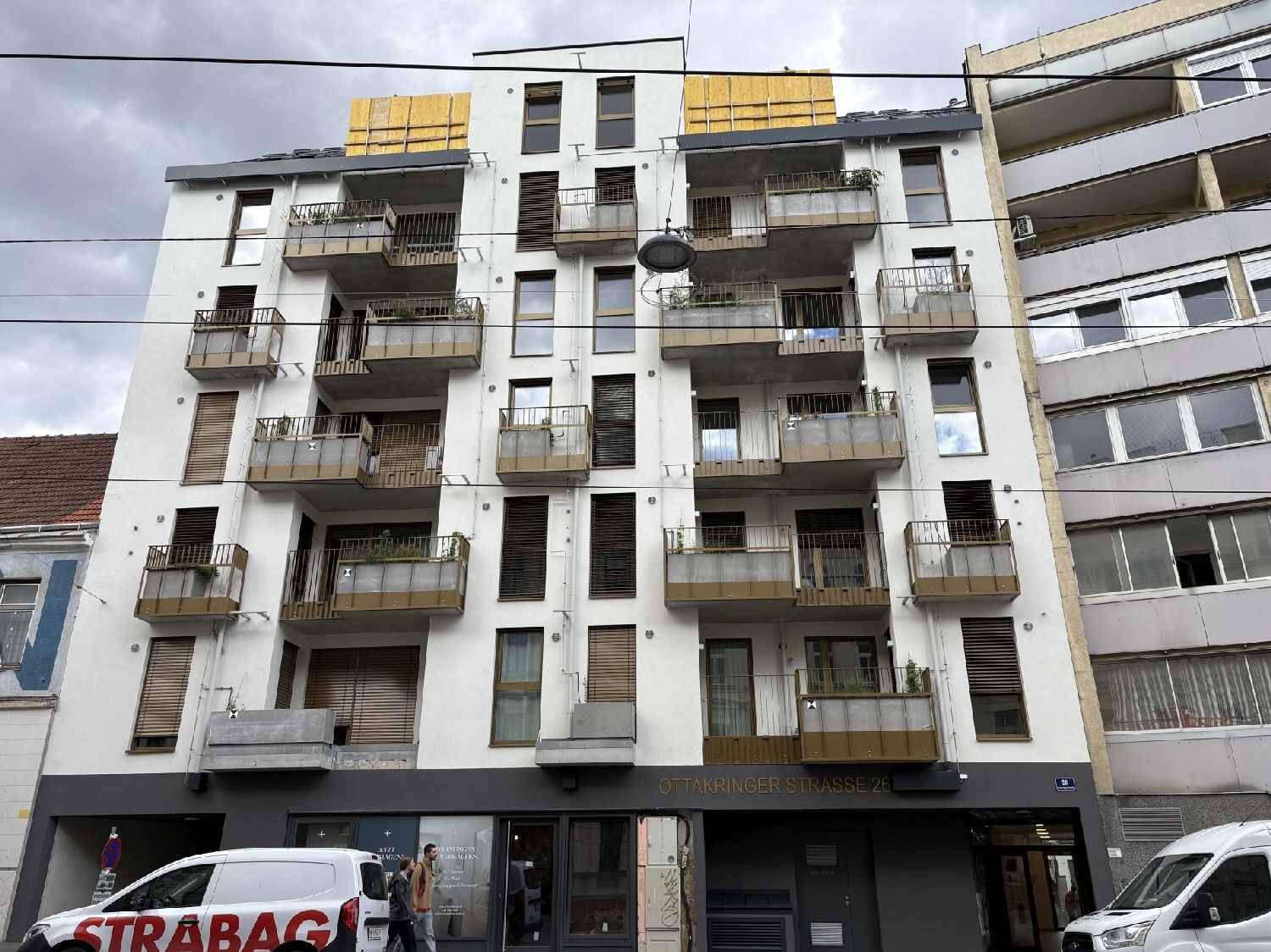 Moderne Wohnhausfassade mit mehreren Balkonen und großen Fenstern an einer Stadtstraße.