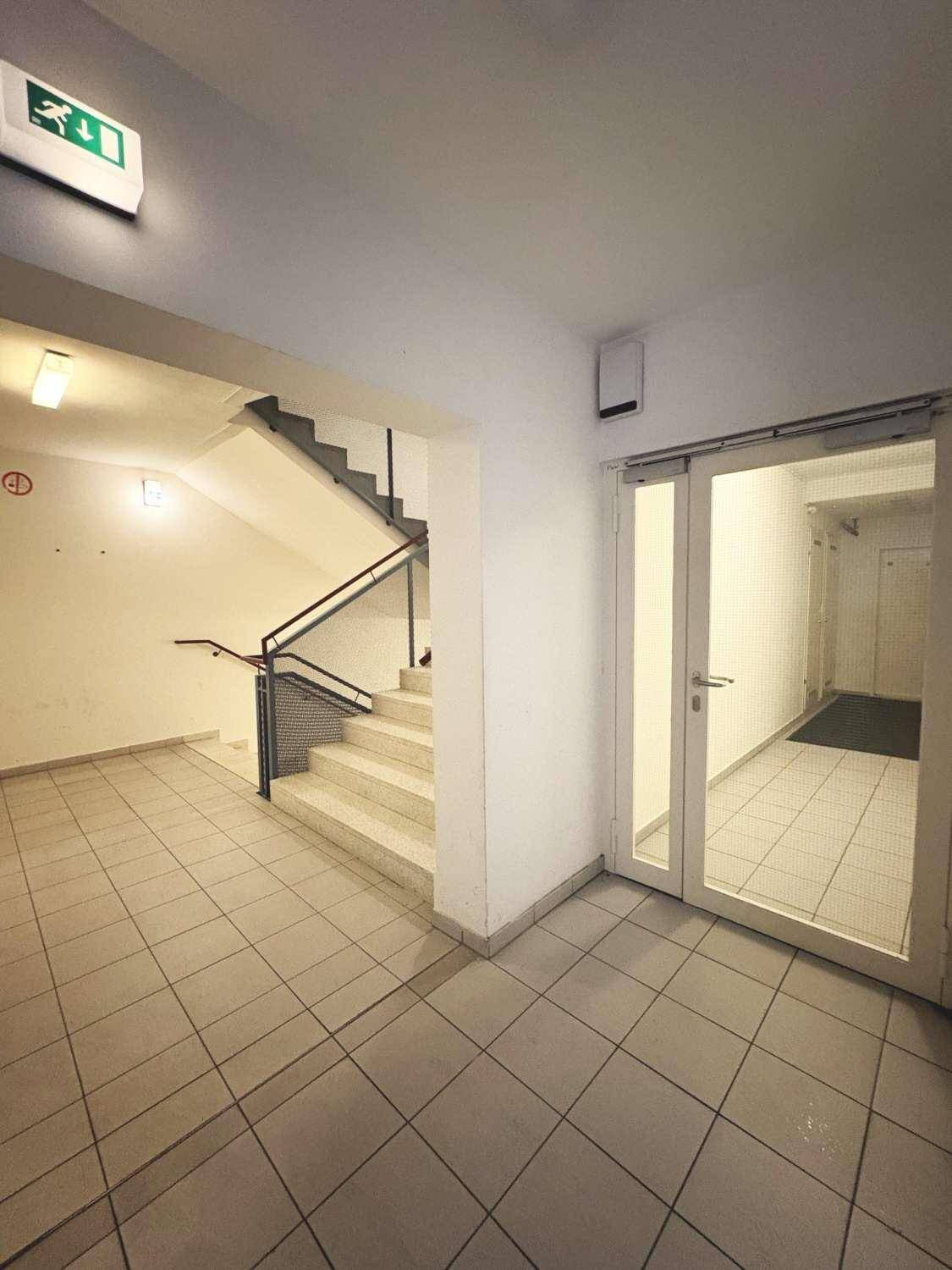 Helles Treppenhaus mit Fliesenboden, Geländer und einem Ausgangsschild.