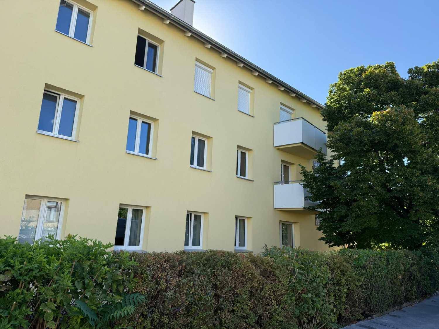 Gelbe Fassade eines Mehrfamilienhauses mit mehreren Fenstern und Balkonen.