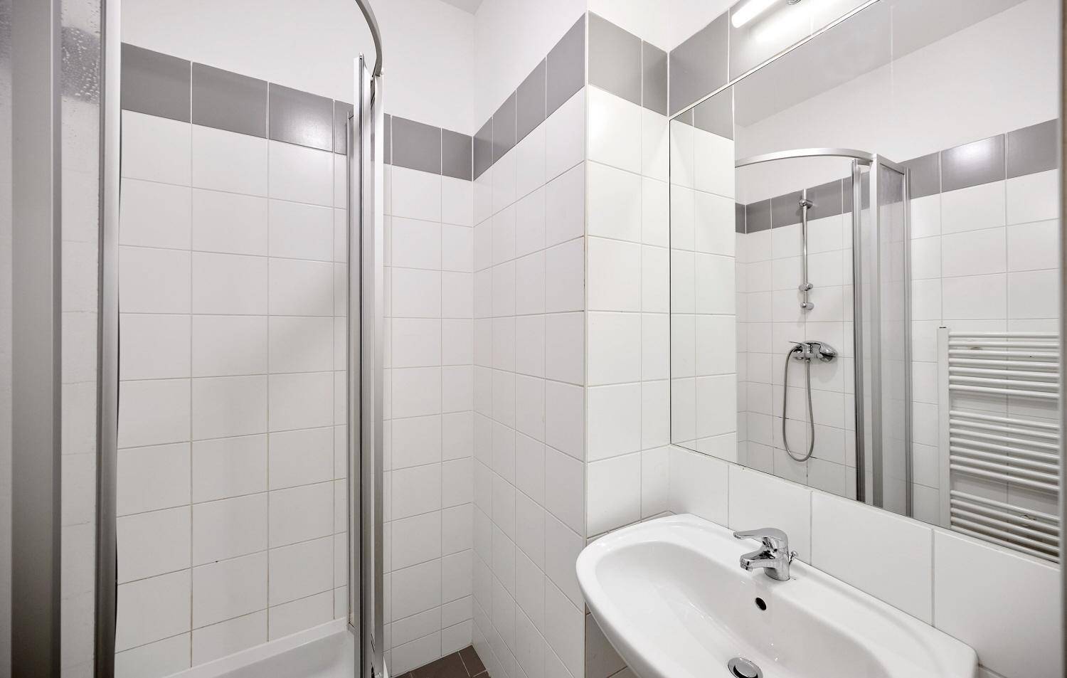 Badezimmer mit Duschkabine, Waschbecken und Spiegel, sowie einem beheizten Handtuchhalter.