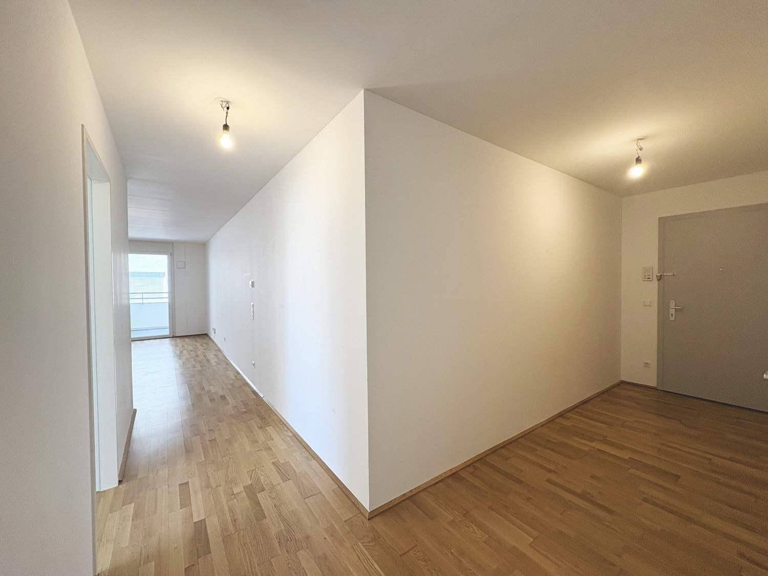 Heller Eingangsbereich mit Holzboden, der zum Wohnbereich und zur Wohnungstür führt.