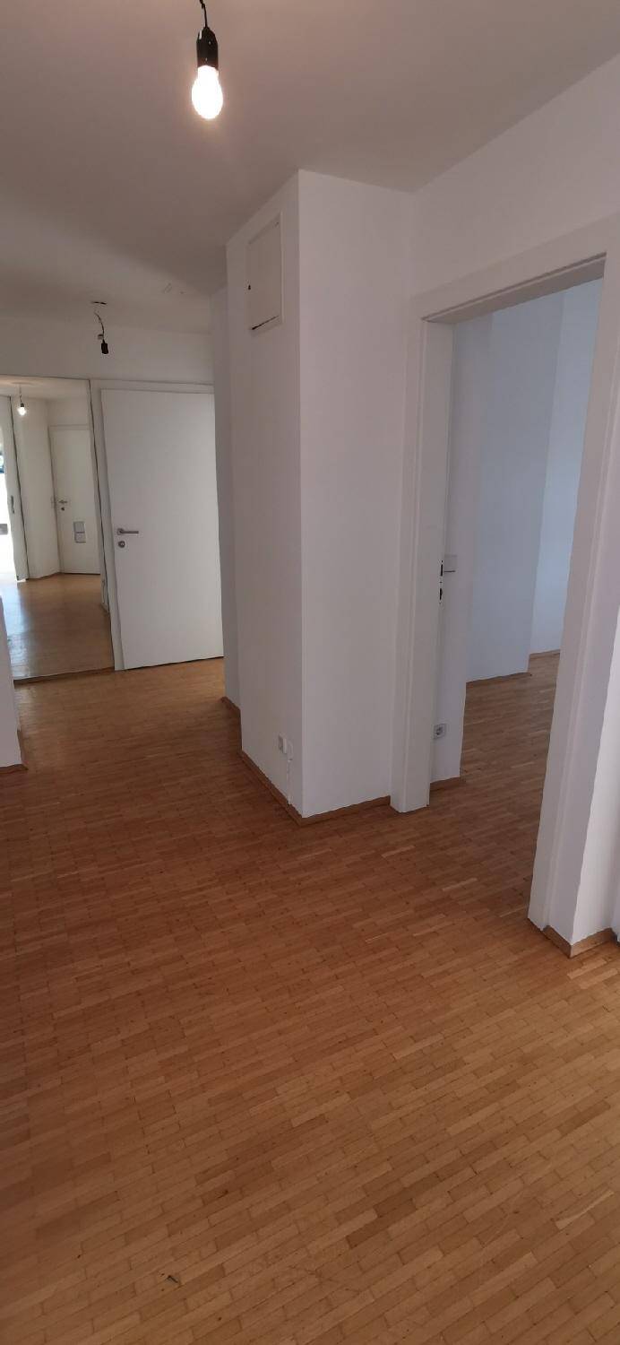 Heller Flur mit Holzparkett und weißen Wänden, der zu weiteren Räumen führt.