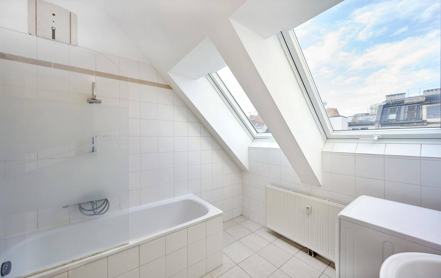 Helles Badezimmer mit Badewanne, weißen Fliesen und drei Dachfenstern für eine angenehme Atmosphäre.