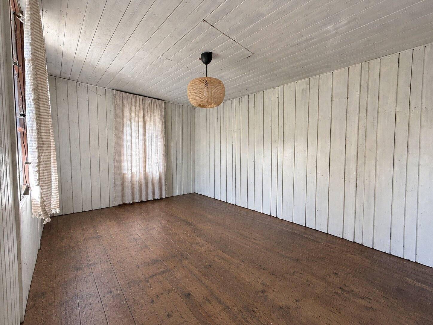 Rustikaler Raum mit weiß getäfelten Wänden und Decke sowie dunklem Holzdielenboden.