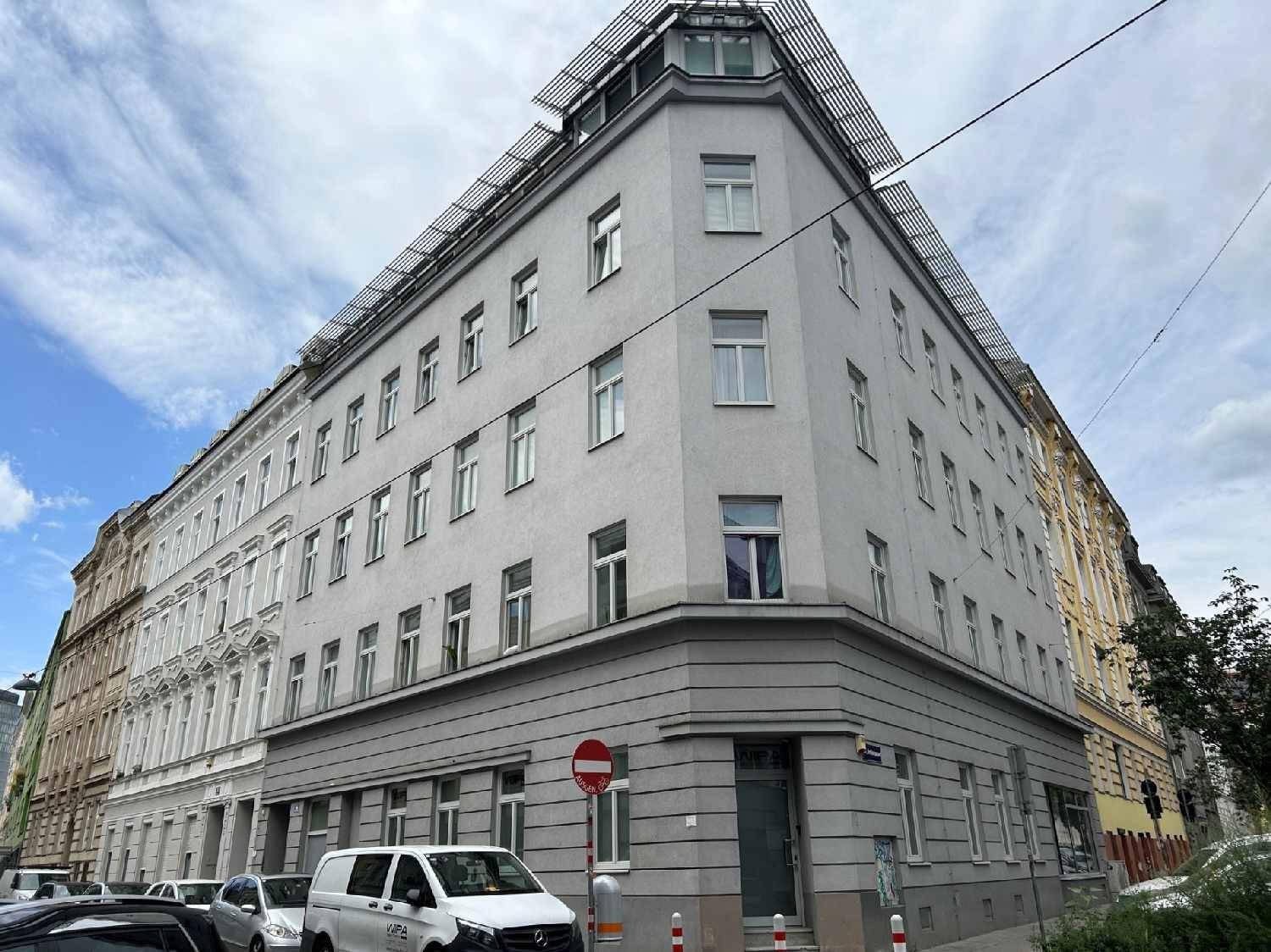 Eckgebäude in städtischer Umgebung mit mehreren Stockwerken und klassischen Fenstern.