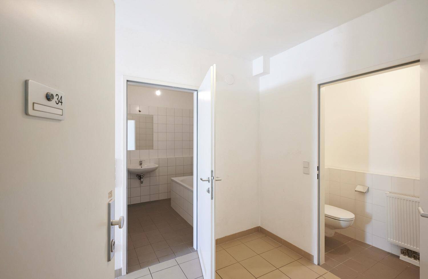 Flur mit Zugang zu separatem Badezimmer und WC, beide mit Fliesenboden.