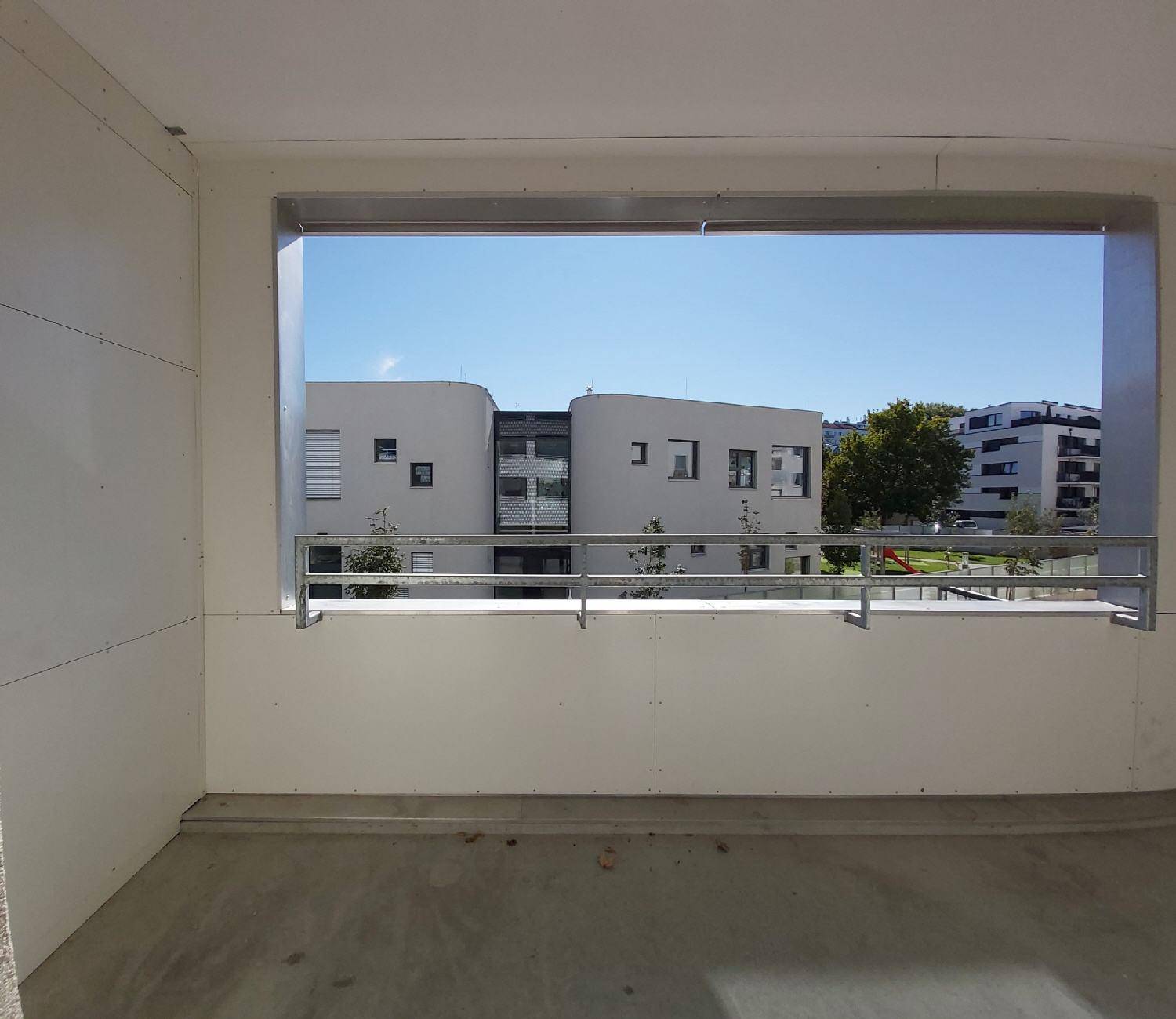 Balkon mit Blick auf die moderne Wohnanlage und einen Spielplatz im Hintergrund.