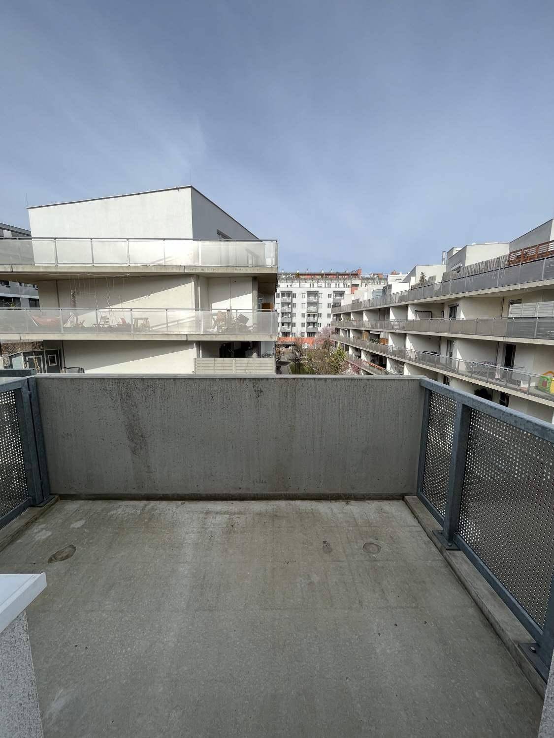 Balkon mit Betonboden und Metallgeländer, bietet einen weiten Blick auf die umliegenden Wohngebäude.