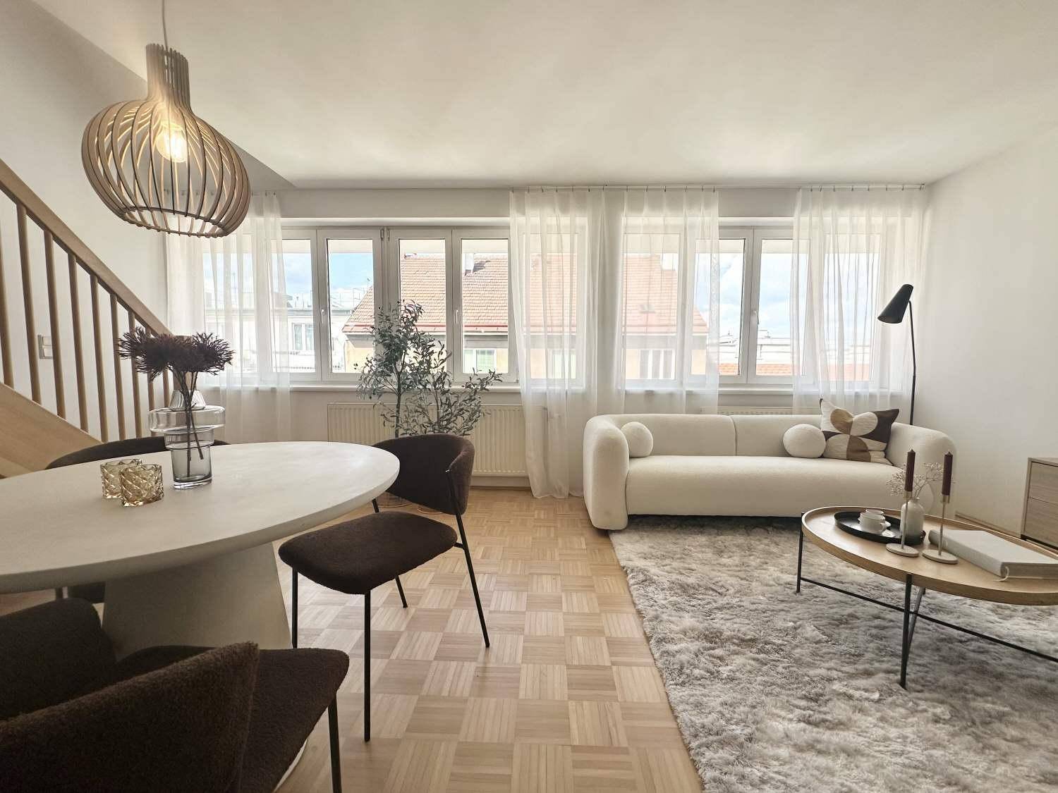 Heller Wohn- und Essbereich mit Parkettboden, bequemer Couch und modernem Esstisch unter einer Lampe.