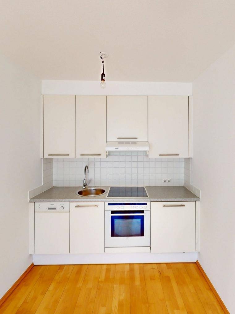 Kompakte Einbauküche mit weißen Schränken, Spülmaschine, Backofen und Induktionskochfeld.