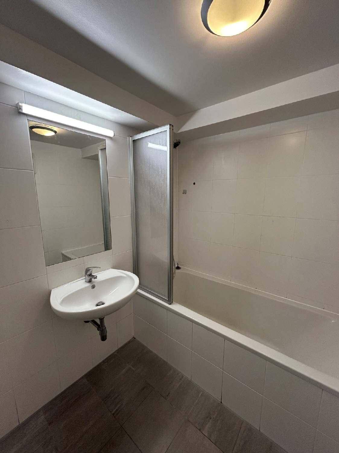Funktionales Badezimmer mit weißen Fliesen, Badewanne mit Duschwand und einem einzelnen Waschbecken.