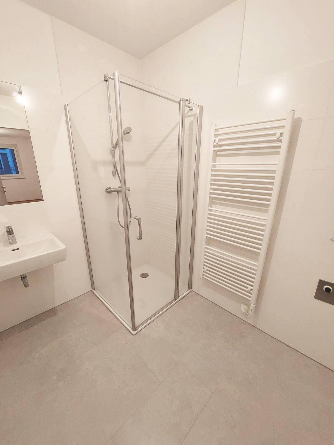 Modernes Badezimmer mit Duschkabine, Waschbecken und beheiztem Handtuchhalter.