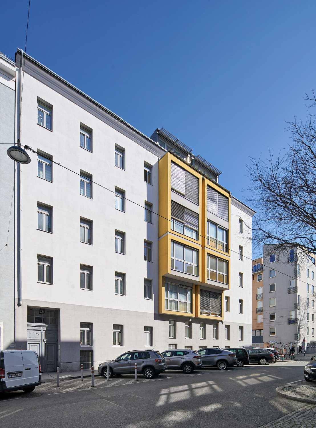 Gebäudeansicht von der Seite mit gelben Fassadenelementen und einer Reihe geparkter Fahrzeuge.