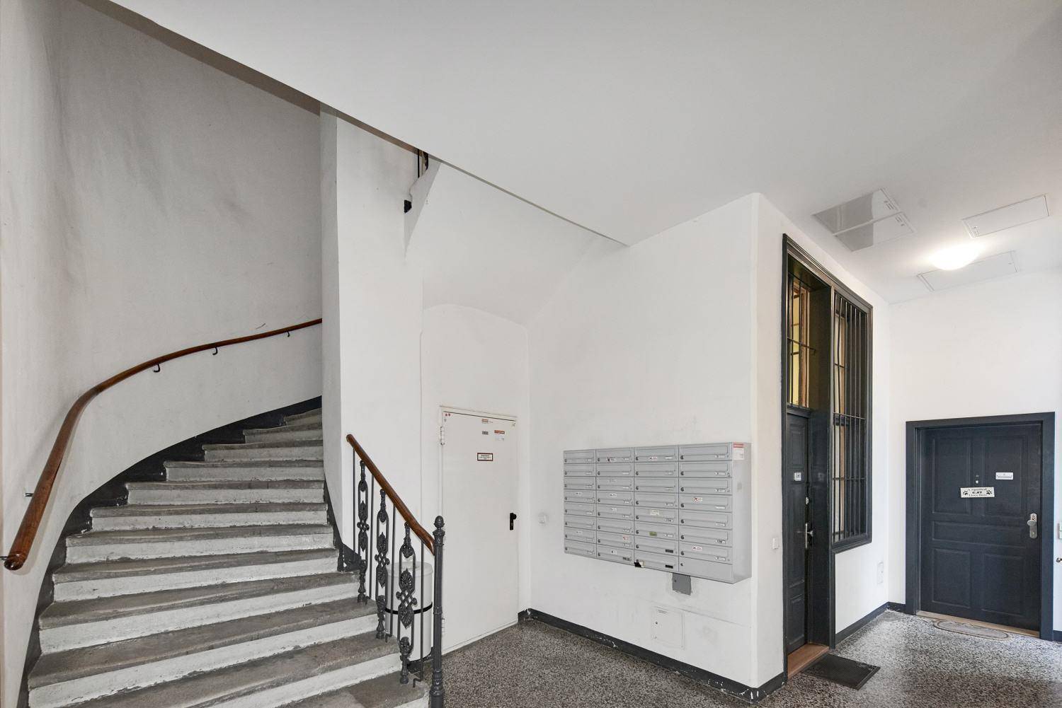 Treppenhaus mit geschwungener Treppe, Terrazzoboden und Briefkästen im Eingangsbereich.
