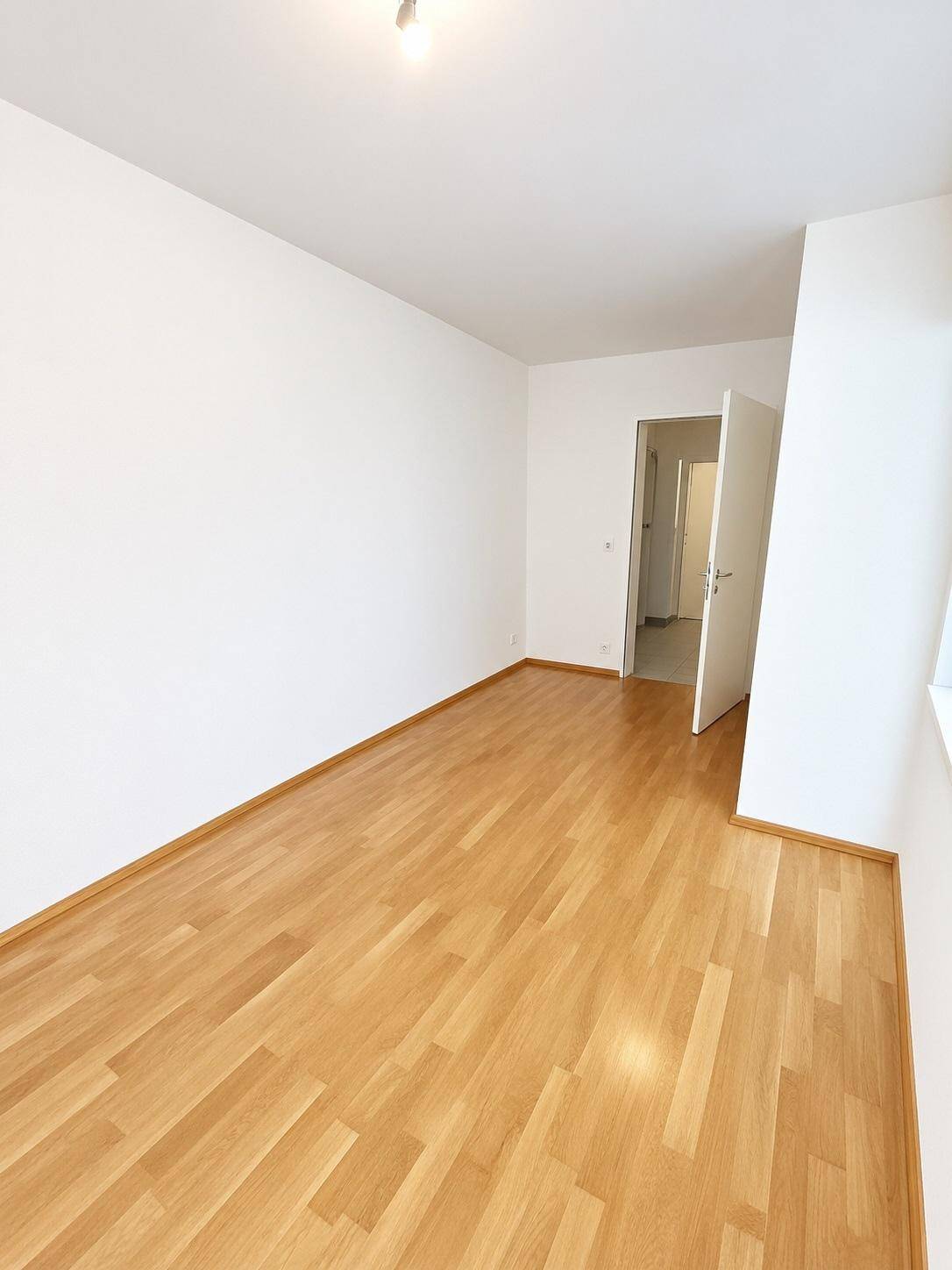 Leeres Zimmer mit hellem Parkettboden und weißen Wänden, bereit zur individuellen Gestaltung.
