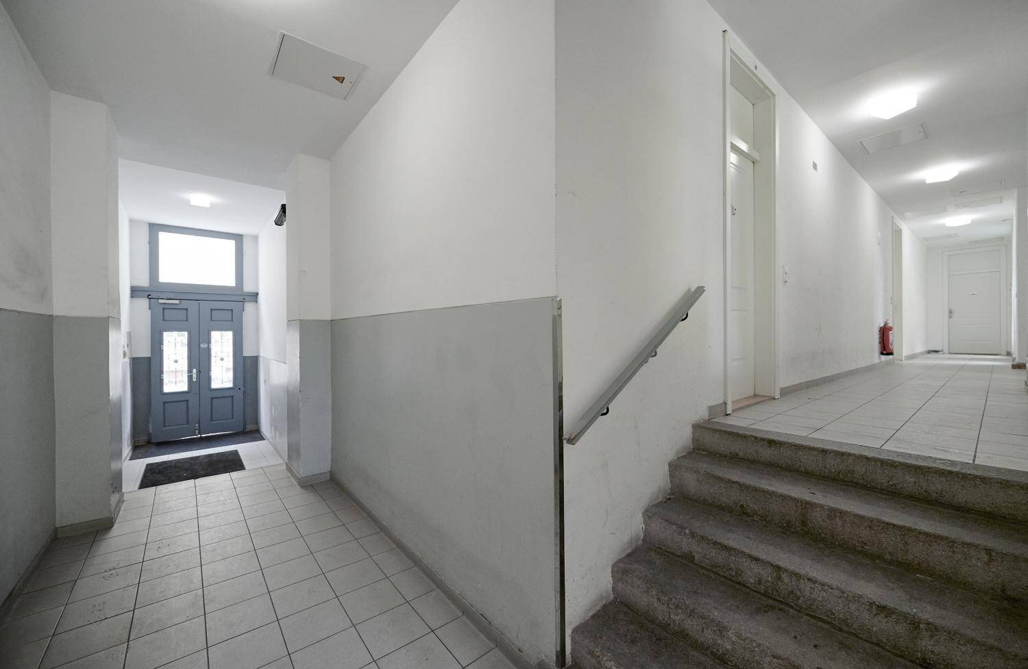 Langer Flur mit Fliesenboden und Zugang zu einem Treppenhaus sowie einem weiteren Eingangsbereich.