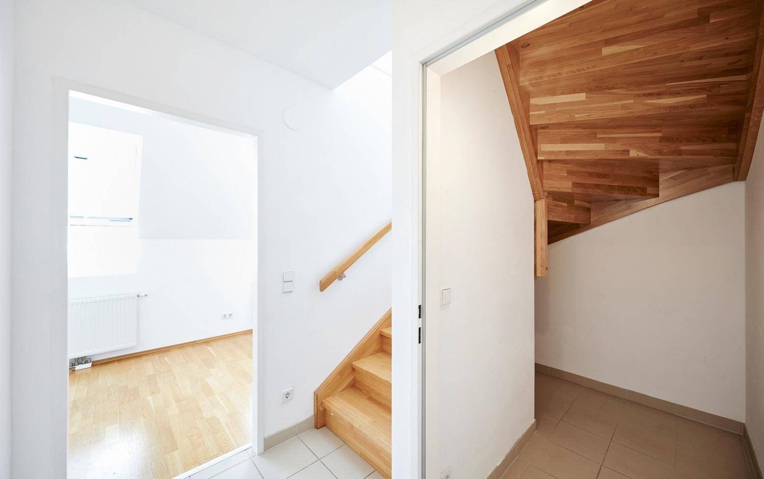 Eingangsbereich mit Holztreppe, die in die obere Etage führt, und Fliesenboden.