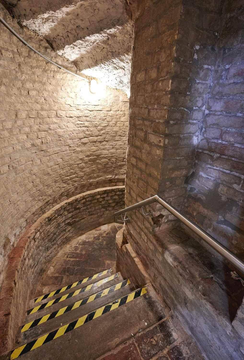 Wendeltreppe in einem alten Keller mit Ziegelwänden und Metallgeländer.