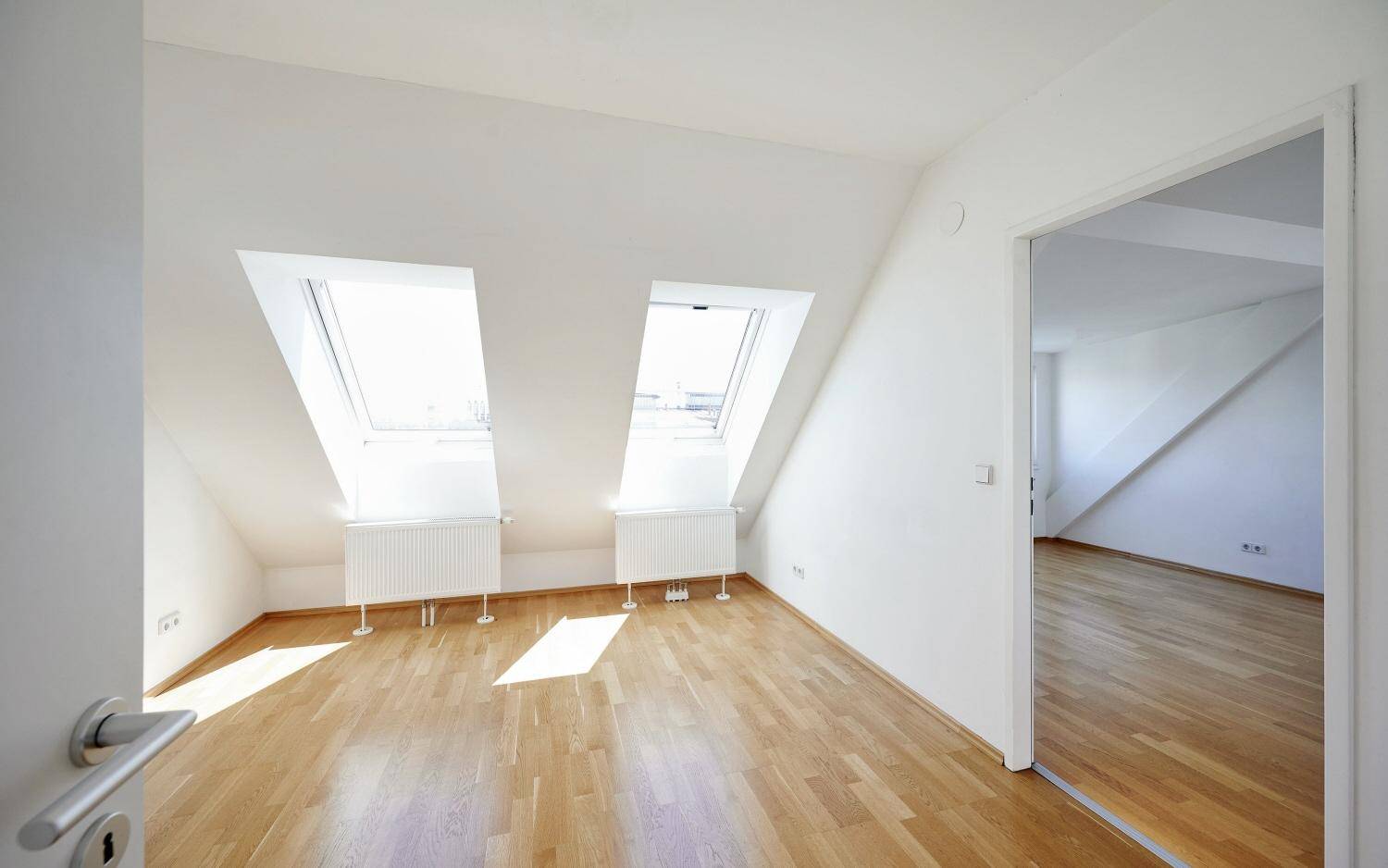 Lichtdurchflutetes Dachzimmer mit Holzboden und zwei großen Dachfenstern, ideal als Schlafzimmer.