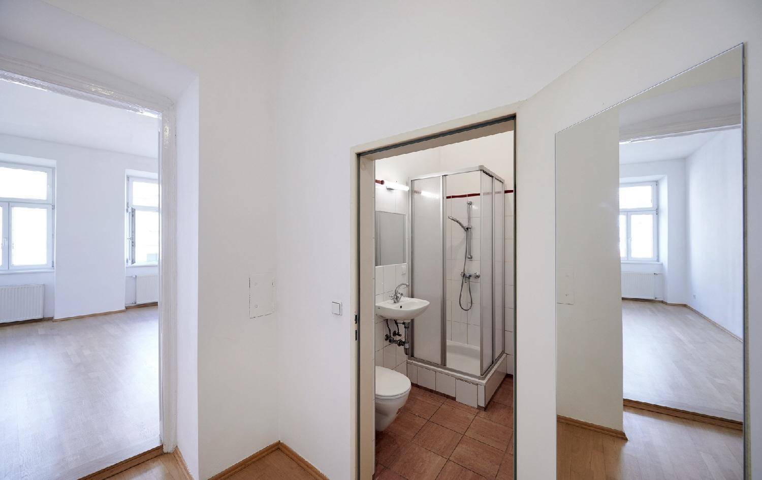 Heller Flur mit Parkettboden, der zu einem kompakten Badezimmer mit Dusche führt.