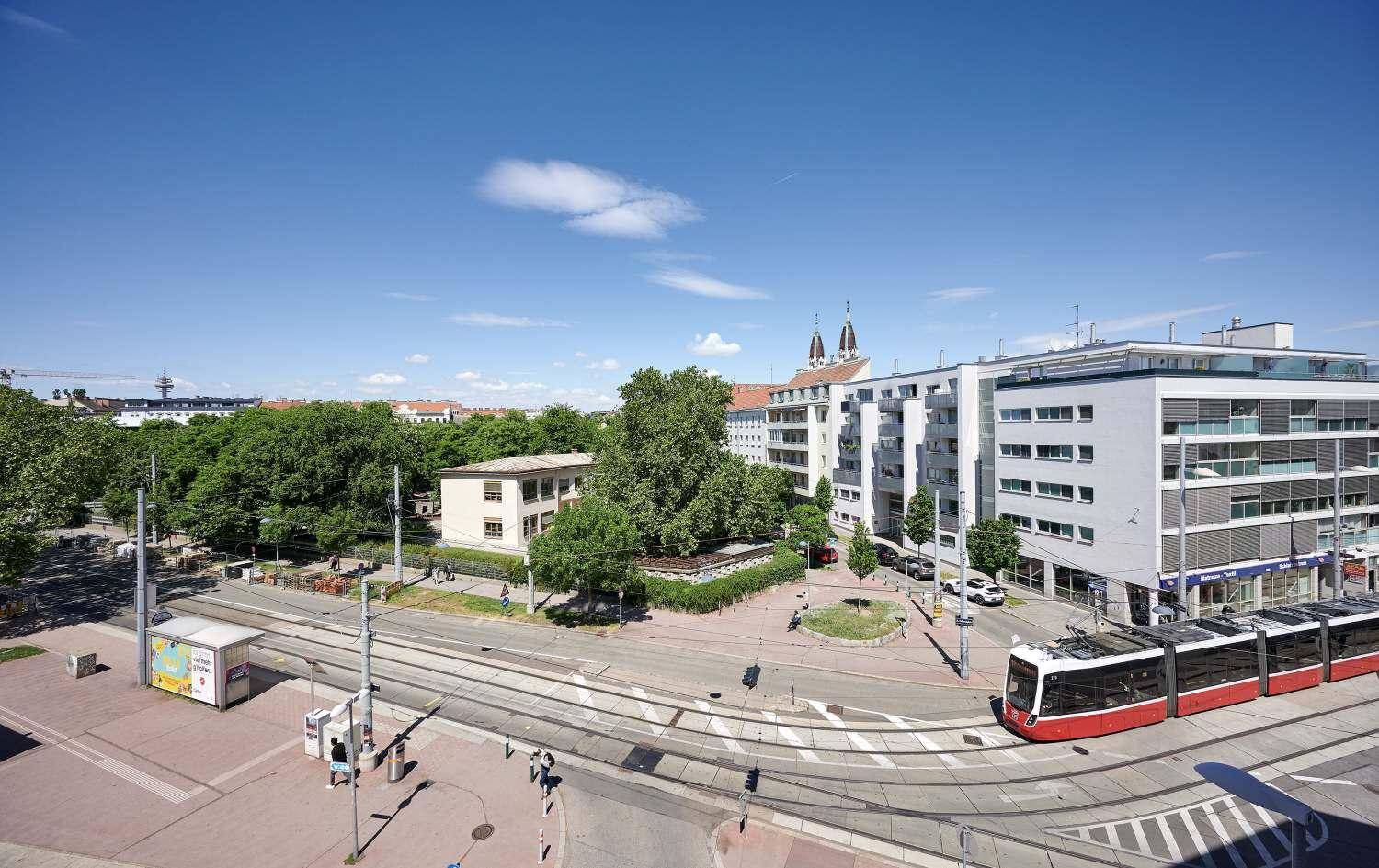 Weitläufige Stadtansicht mit Straßenbahnen, Gebäuden und viel Grün unter blauem Himmel.